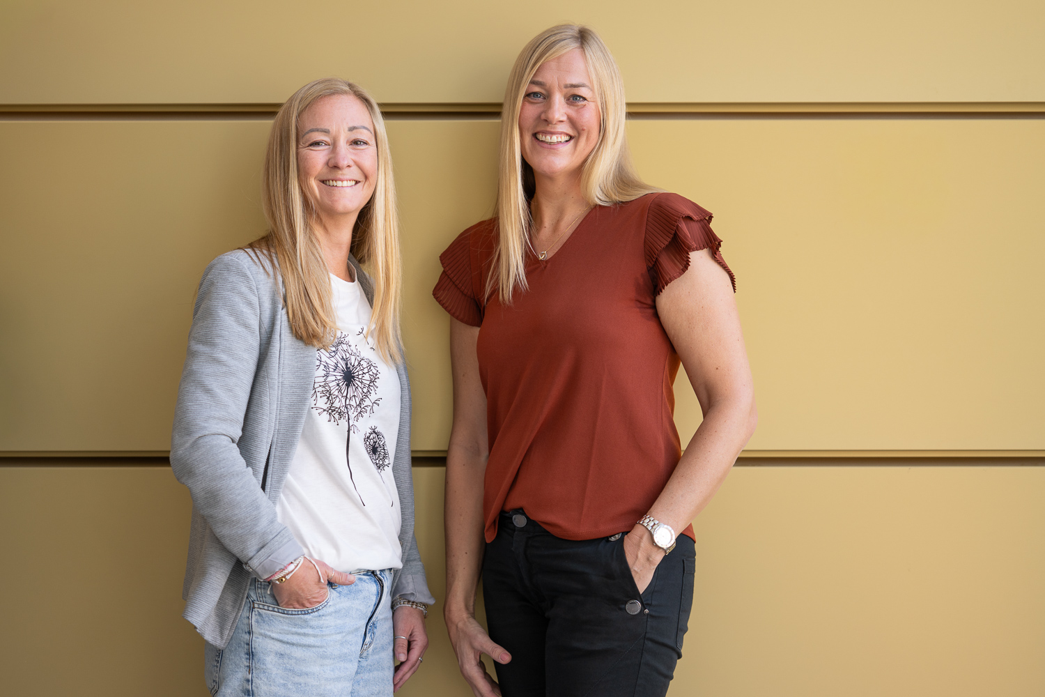 Två personer framför en gul vägg.